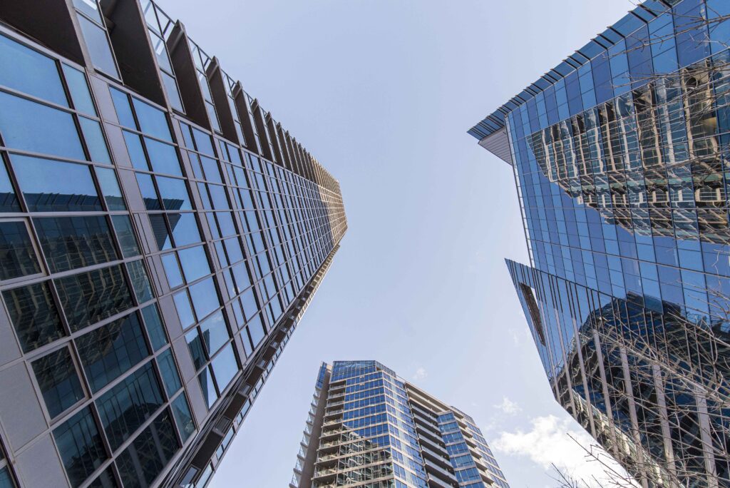 Vista en contrapicado de grandes edificios modernos de cristal que representan el objetivo de la digitalización de telecomunicaciones en fincas y comunidades.
